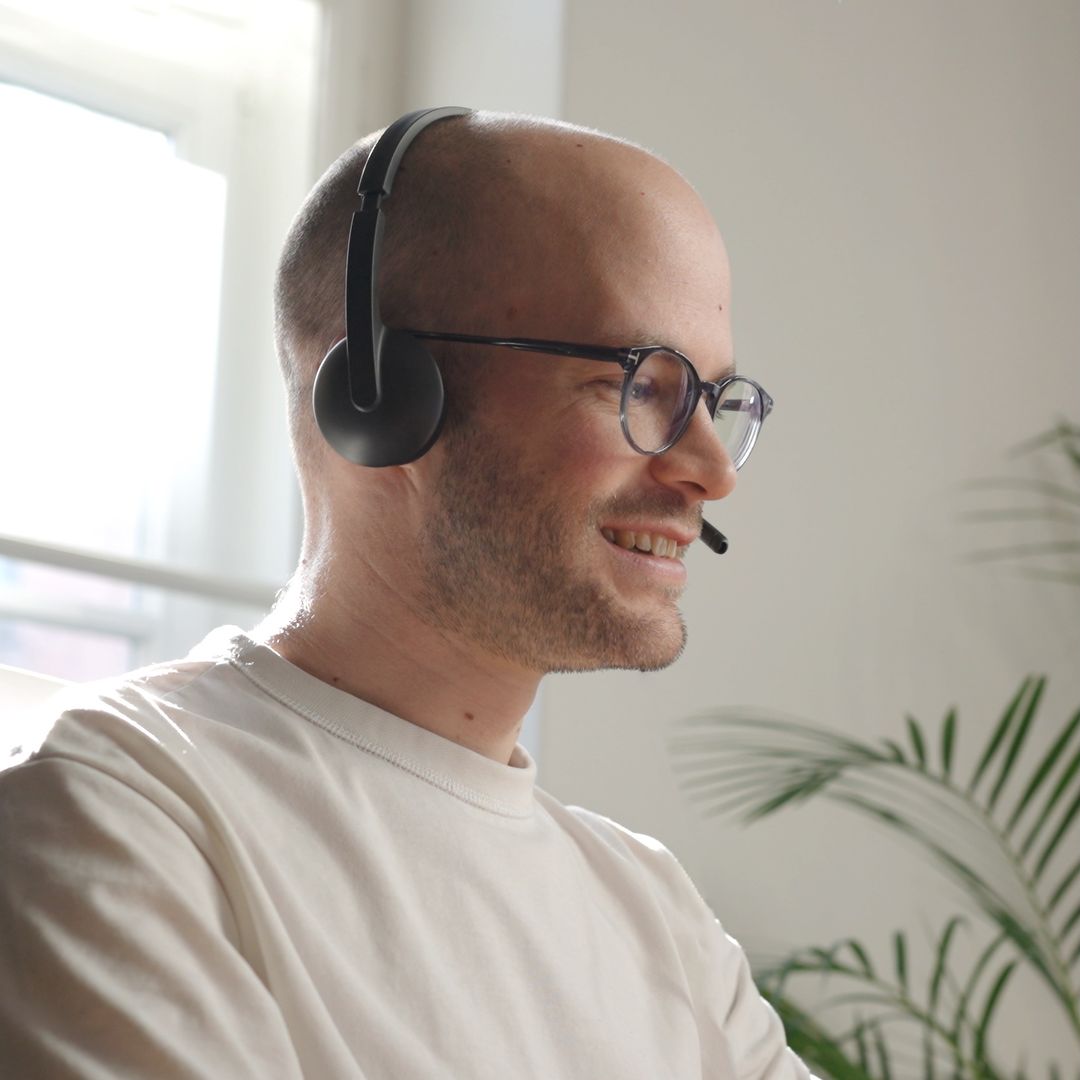 Smiling loomobox customer success team member with headset and glasses during a support call in a bright office