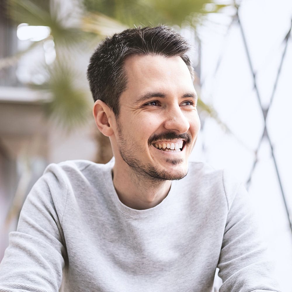 Florian, laughing in a grey sweater with green plants in the background, loomobox team