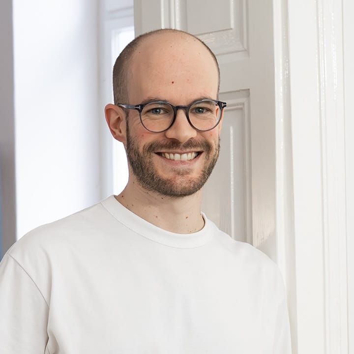 Michael, smiling with round glasses and a white shirt by a bright doorway, loomobox team