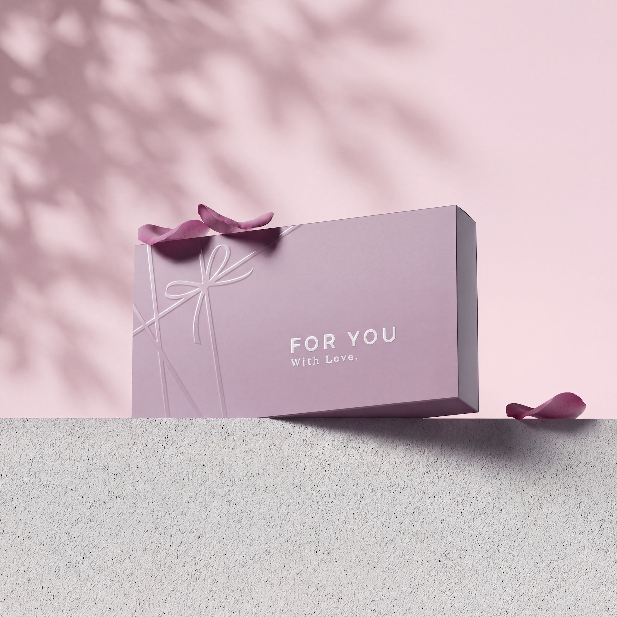 Lilac gift box embossed "FOR YOU With Love." on a stone ledge against a pink wall with leaf shadows and rose petals