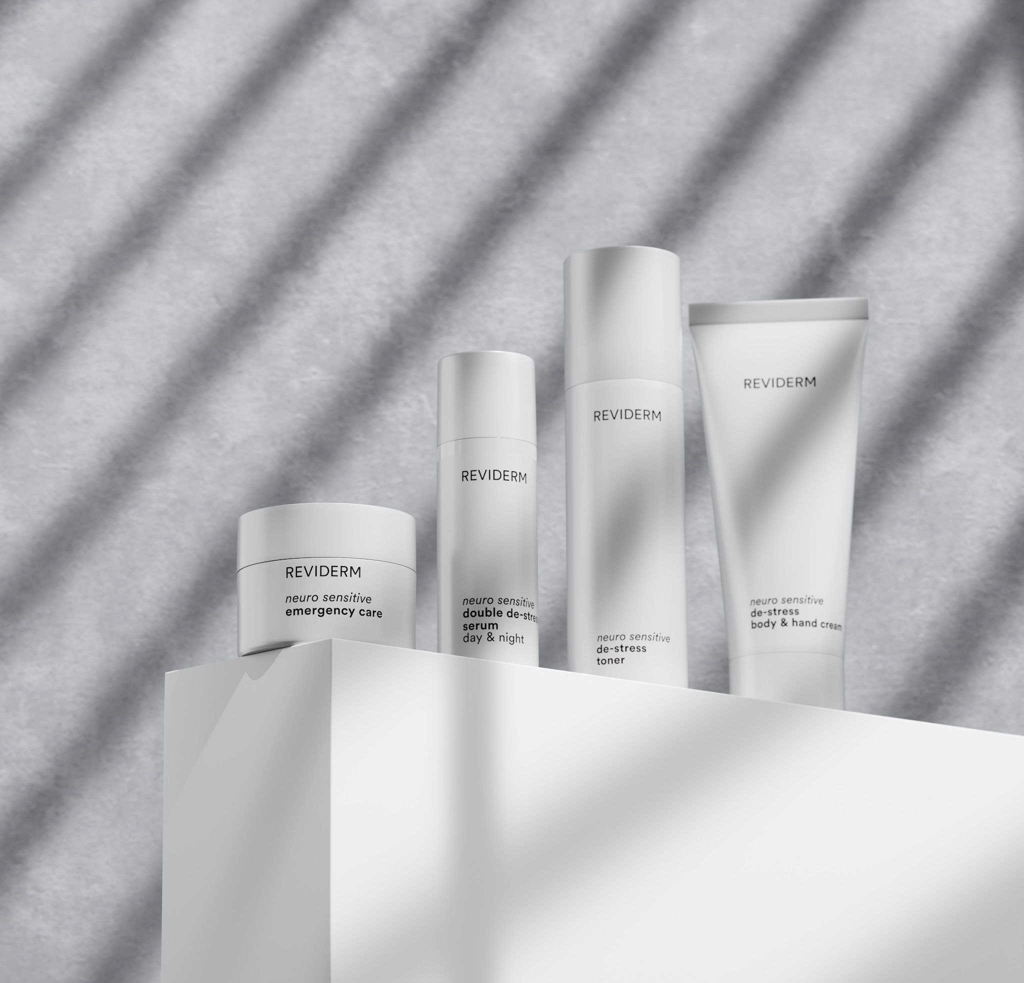 REVIDERM neuro sensitive de-stress line with emergency care, double de-stress serum, de-stress toner and body & hand cream in white packaging with striped shadows