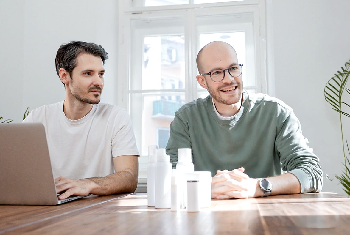 Florian and Michael from the loomobox team at a table with skincare products and a laptop, ready to help