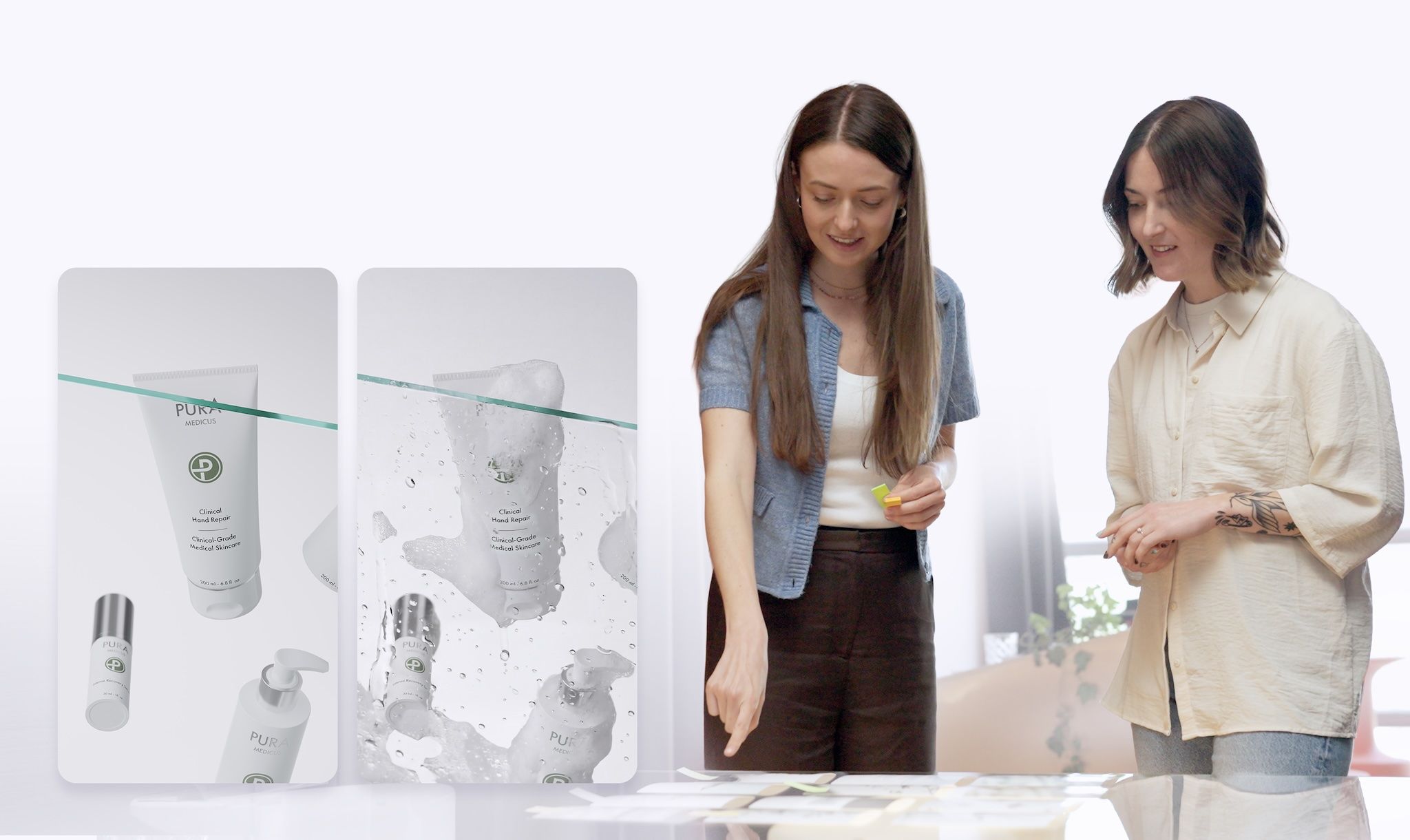 Two loomobox designers reviewing PuraMedicus Clinical Hand Repair renders — one plain, one with a water splash — on a glass table