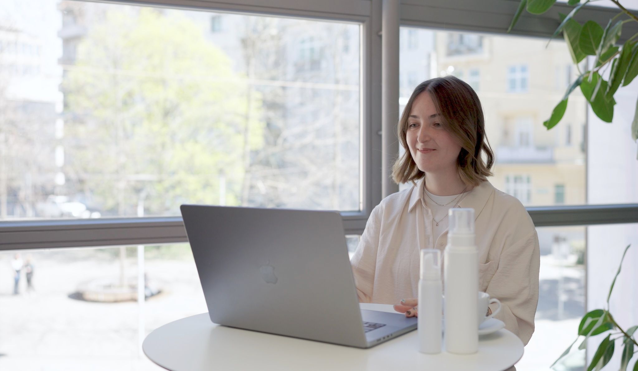 loomobox client working at her laptop by a sunny office window, with two white skincare bottles on the table